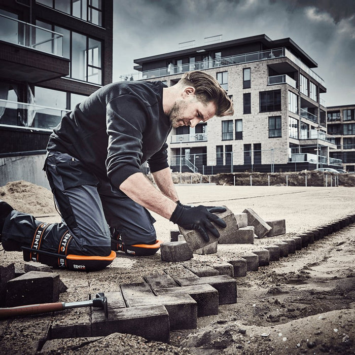 Worn knee pads on a worker kneeling; black shells with orange trim and straps