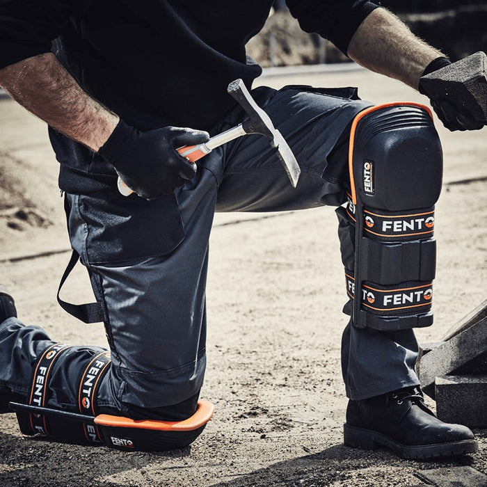Side view of worn knee pads on black work pants; hinged shells with orange trim