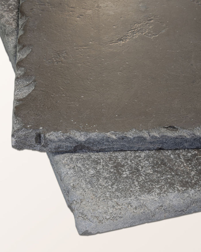 Two Hazlebury Limestone Seasoned Finish tiles stacked to show the tumbled chipped edge profile and honed grey surface