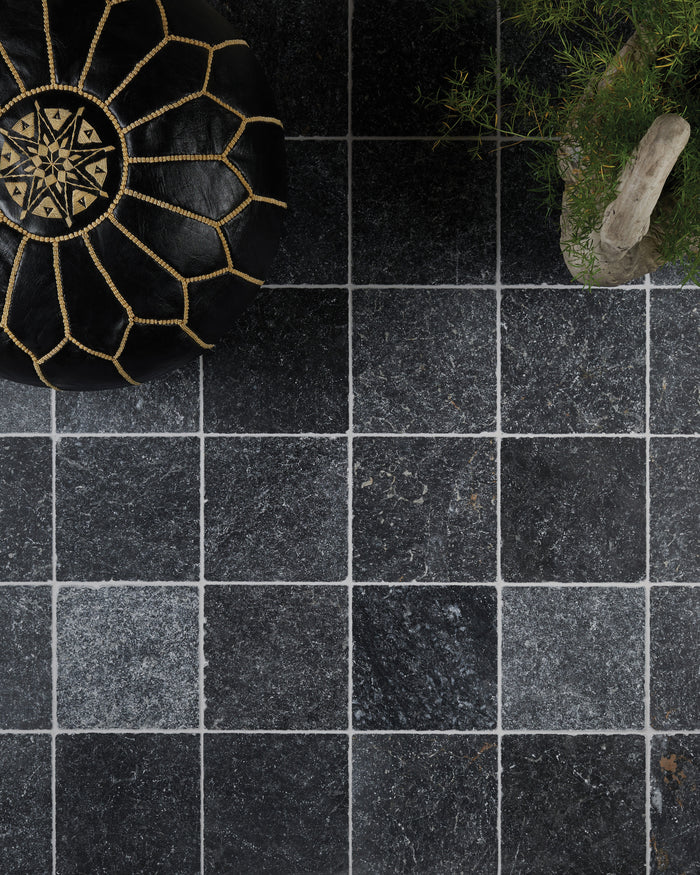 Overhead view of Kendal Marble Tumbled Finish laid square with pale grout, styled with a black and gold Moroccan leather pouffe and an asparagus fern