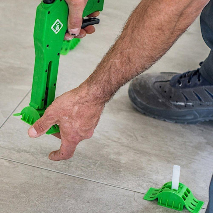 Green installation tool used on floor tiles with hands positioning near the seam