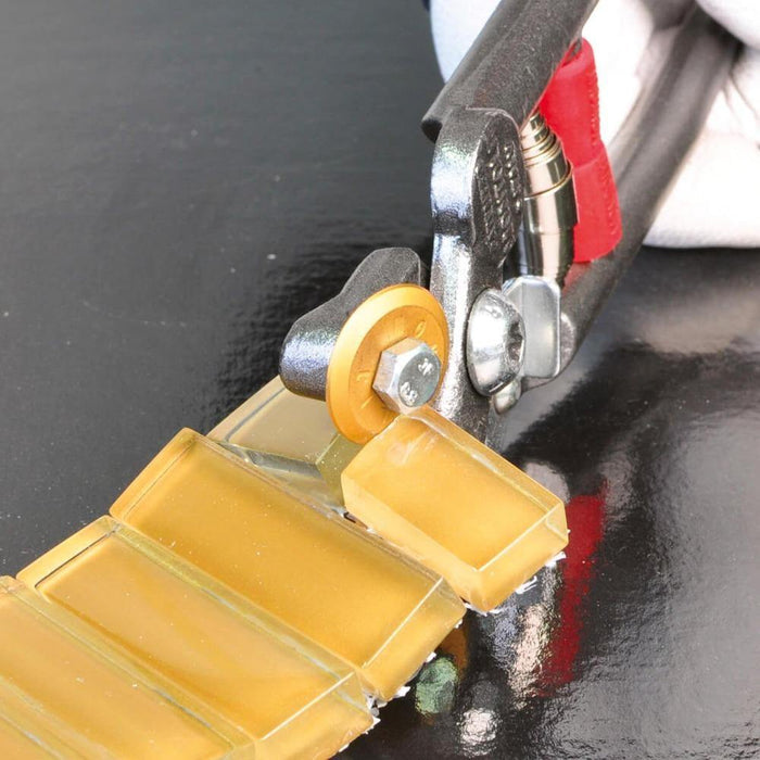 Close-up mosaic nippers: metal jaw clamps yellow guide wheel over tile