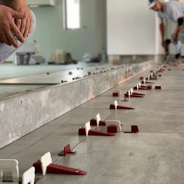 Multiple white T-Lock tile leveling clips with red spacers along tiled floor