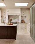 Riviera Limestone Tumbled flagstones running across a country kitchen floor, with a dark oak island, cream shaker cabinetry and a sage green larder cupboard