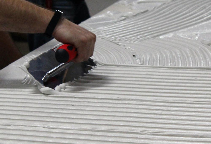 Notch trowel spreading white compound on a surface with sawtooth ridges