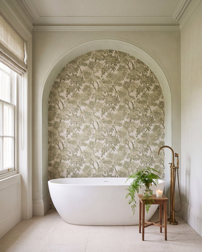 Sanderson Tapestry Trees Forest Mural Porcelain filling an arched alcove behind a freestanding bath, with a brass floor-standing bath tap, a maidenhair fern and pale limestone flooring