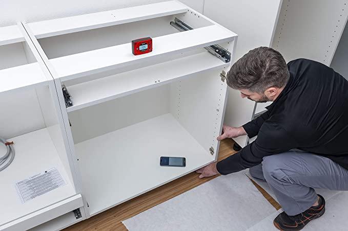 Installer using the red Sola Go digital pocket level to check cabinet shelf level