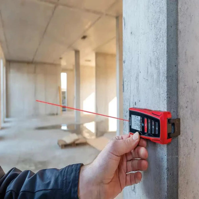 Hand holding red laser distance meter aimed at a wall, laser line visible