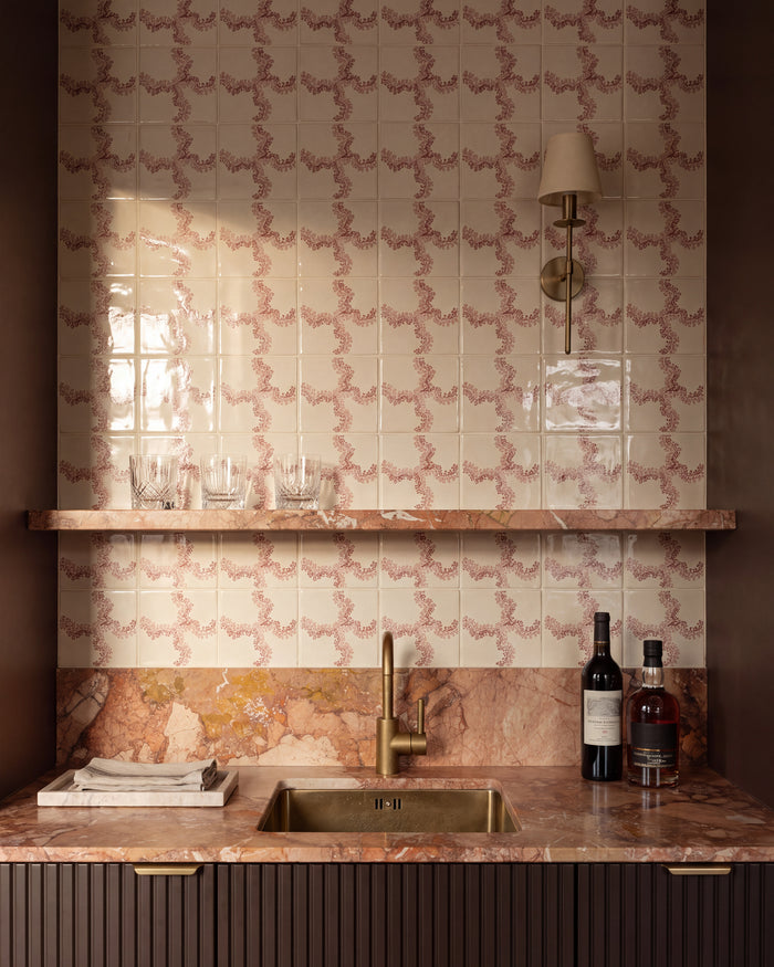 STUDIO Sanderson Oxbow Check Madder tiles behind a drinks bar, with a brass sink and tap, pink marble worktop and shelf, fluted cabinetry and a slim brass wall light