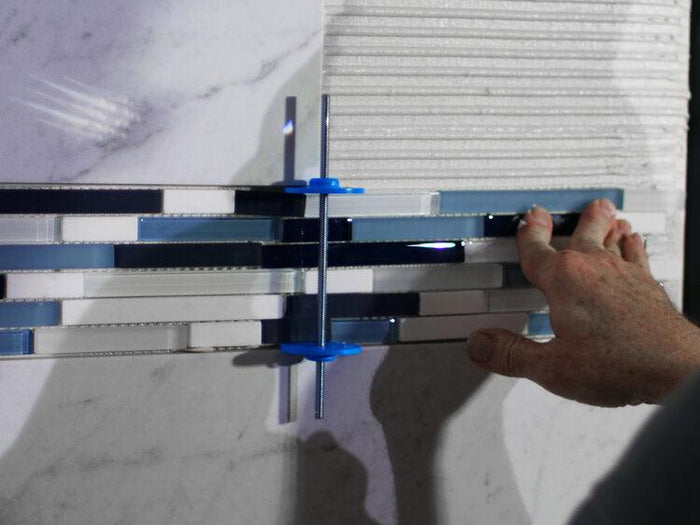 Adjustable tile inlay spacer being used between tiles with blue leveling pins