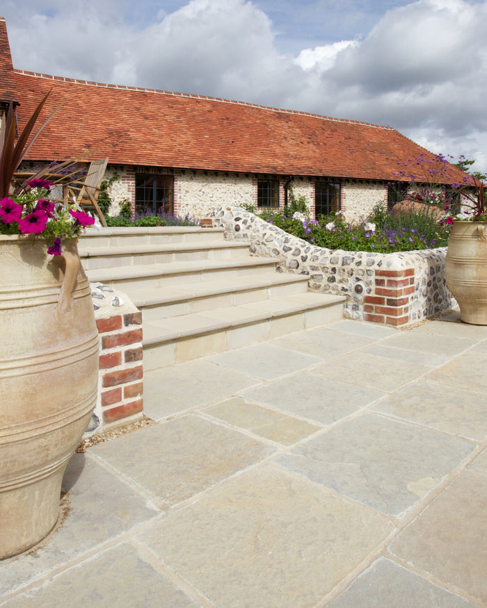 Trusloe Limestone Seasoned Finish paving and steps on a flint-walled garden terrace with planted borders