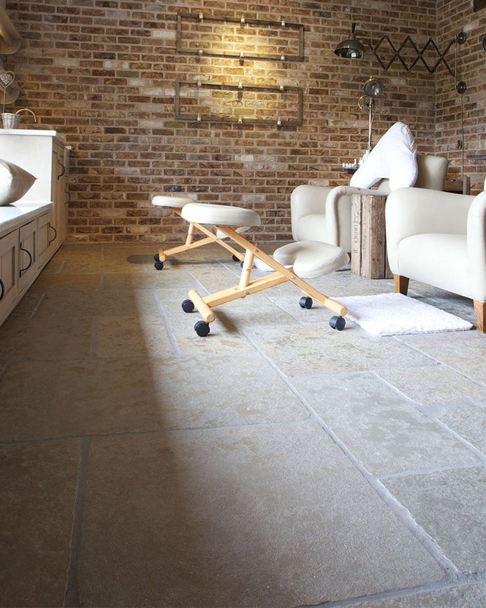 Trusloe Limestone Seasoned Finish flagstone floor in a relaxed brick-walled room with cream armchairs