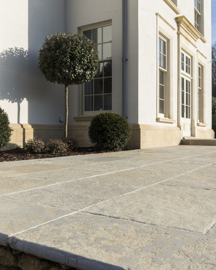 Trusloe Limestone Seasoned Finish paving laid in wide bands outside a white rendered house with clipped topiary