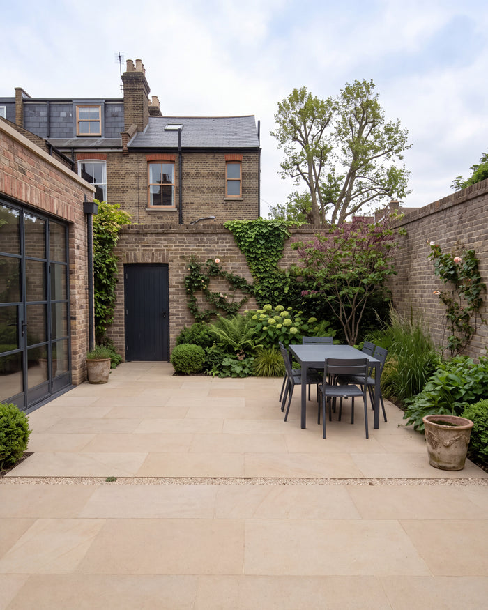 Wensley York Sandstone Honed paving in an enclosed town garden with Crittall doors, a dark metal dining table and climbing roses on the brick walls