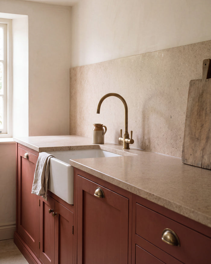 Wychwood Limestone Honed Slab as a 3cm kitchen worktop with a matching full height splashback, above terracotta red cabinetry with a butler sink and aged brass tap